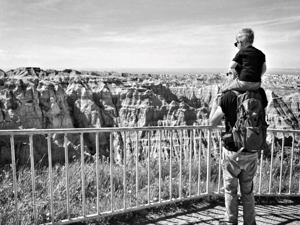 Black and white kid on dad's shoulders looking at badlands